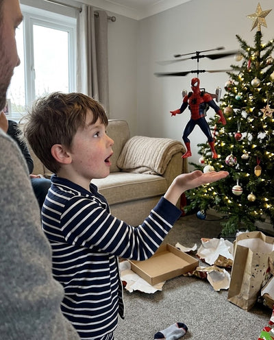 Boy hovering a Spider-Man FlyHero Pro above his open palm by a Christmas tree